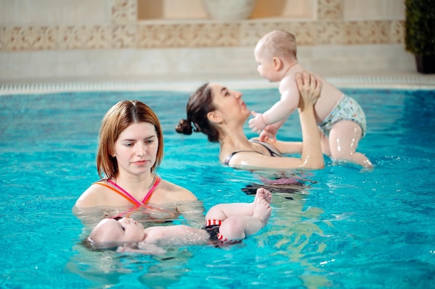 Un gruppo di madri con i loro bambini piccoli in una lezione di nuoto per bambini con un allenatore.