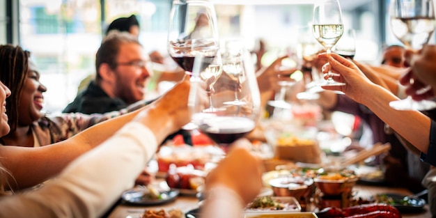 Un gruppo di persone diverse che battono i bicchieri in una riunione vivace Celebrazione con gli amici che condividono gioia e risate Applausi a un pasto festivo che si godono insieme Gli amici che festeggiano e brindano
