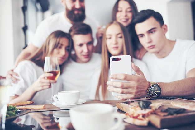 Un gruppo di persone fa una foto selfie in un caffè. I migliori amici si sono riuniti a tavola per mangiare la pizza e cantare vari drink