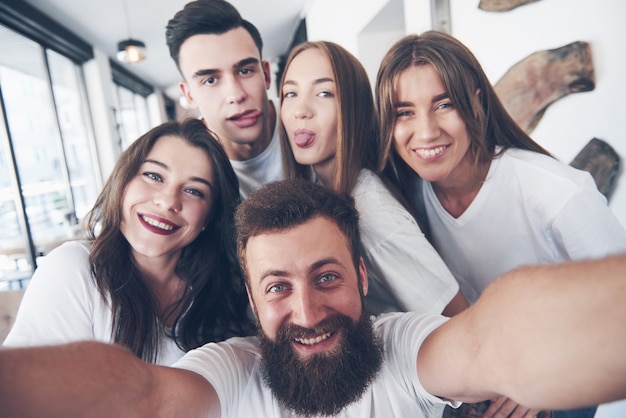 Un gruppo di persone fa una foto selfie in un caffè. I migliori amici si sono riuniti a tavola per mangiare la pizza e cantare vari drink