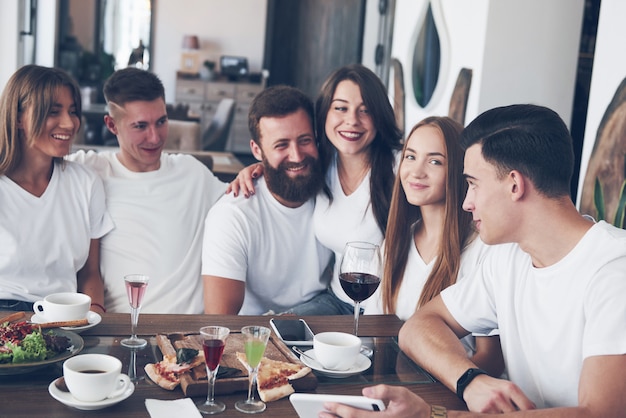 Un gruppo di persone fa una foto selfie in un caffè. I migliori amici si sono riuniti a tavola per mangiare la pizza e cantare vari drink