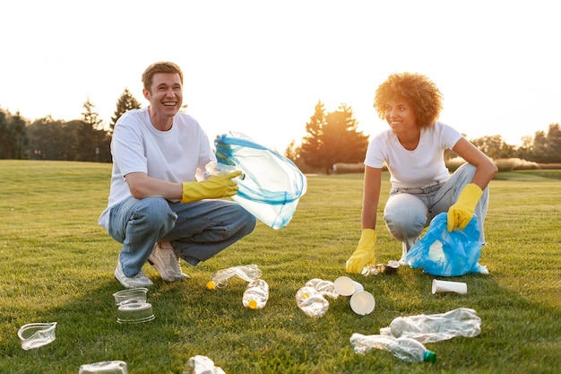 un gruppo di persone multirazziali con guanti e sacchetti della spazzatura rimuovono la plastica e la spazjatura nel parco