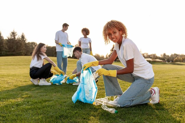 un gruppo di persone multirazziali con guanti e sacchetti della spazzatura rimuovono la plastica e la spazjatura nel parco