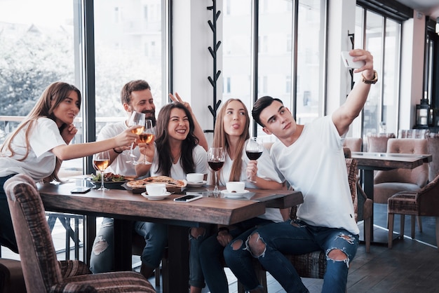 Un gruppo di persone scatta una foto selfie in un bar. I migliori amici si sono riuniti a tavola mangiando pizza e cantando vari drink.