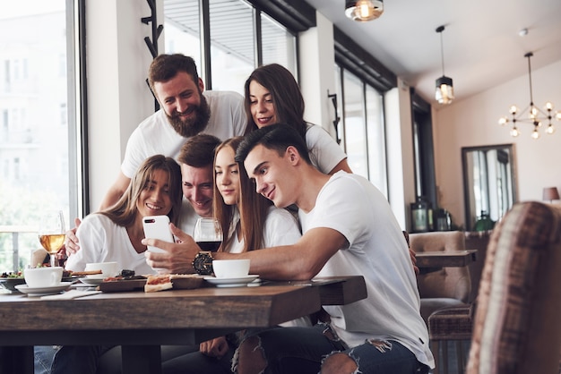 Un gruppo di persone scatta una foto selfie in un bar. I migliori amici si sono riuniti a tavola mangiando pizza e cantando vari drink.