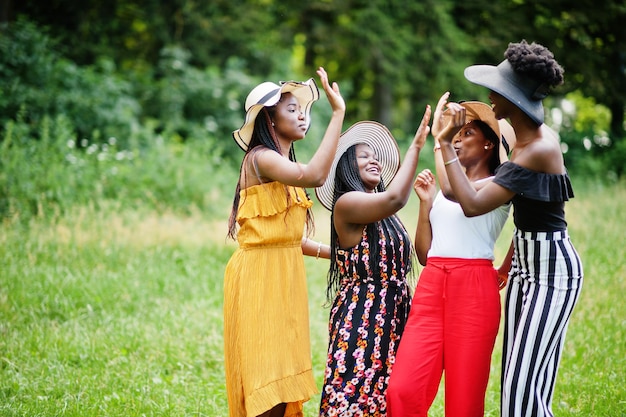 Un gruppo di quattro bellissime donne afroamericane indossano un cappello estivo trascorrendo del tempo sull'erba verde nel parco.