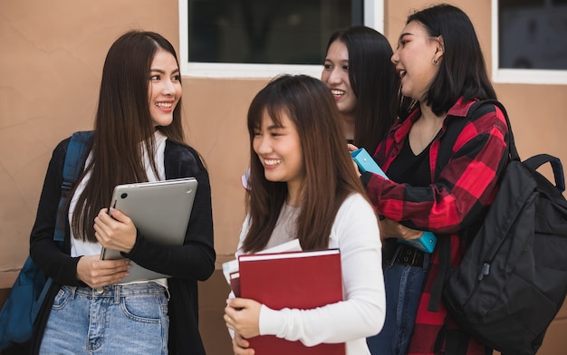 Un gruppo di quattro giovani studenti universitari attraenti ragazze asiatiche in piedi insieme parlando nel campus universitario. Concetto per l'istruzione e la vita degli studenti universitari.