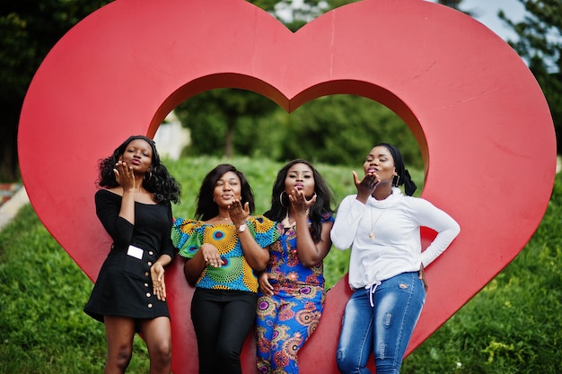 Un gruppo di quattro ragazze afroamericane contro il grande cuore rosso all'aperto inviando baci d'aria