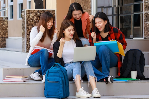 Un gruppo di quattro ragazze studentesse di college che tengono libri e computer notebook seduti e parlano insieme