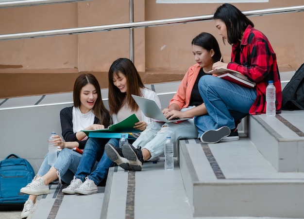 Un gruppo di quattro studenti universitari asiatici attraenti seduti su ogni scalinata nel campus universitario che studiano all'aperto. Concetto per l'istruzione, l'amicizia e la vita degli studenti universitari.