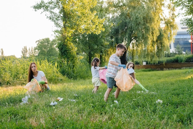 Un gruppo di ragazze con bambini al tramonto è impegnato nella raccolta dei rifiuti nel parco. Cura dell'ambiente, riciclaggio.