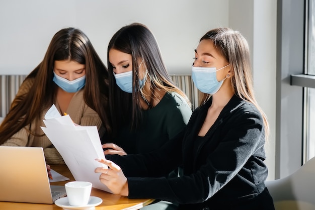 Un gruppo di ragazze in maschera si siede in un bar e lavora sui laptop. Insegnare agli studenti.