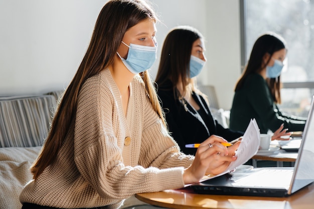 Un gruppo di ragazze mascherate mantiene una distanza sociale in un bar quando lavora al laptop.