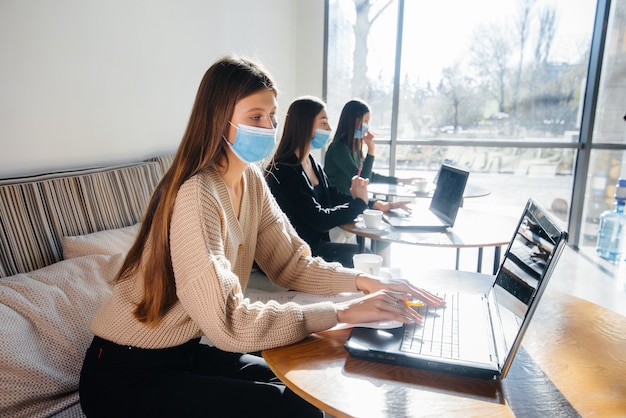 Un gruppo di ragazze mascherate mantiene una distanza sociale in un bar quando lavora al laptop.