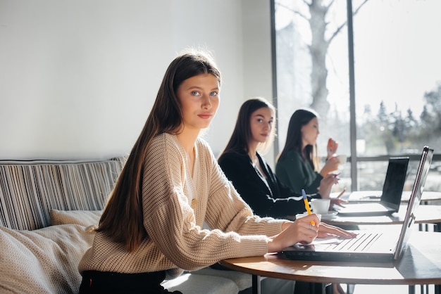 Un gruppo di ragazze si siede in un ufficio al computer e discute dei progetti. Comunicazione e formazione online.