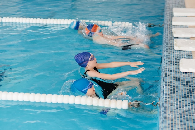 Un gruppo di ragazzi e ragazze si allena e impara a nuotare in piscina con un istruttore. Sviluppo di sport per bambini.