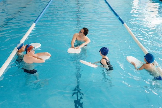 Un gruppo di ragazzi e ragazze si allena e impara a nuotare in piscina con un istruttore. Sviluppo di sport per bambini.