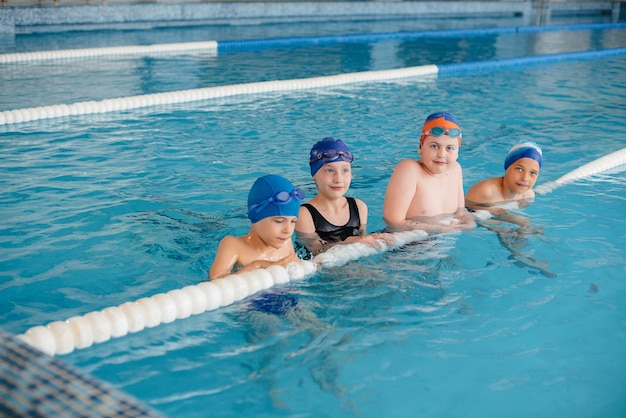 Un gruppo di ragazzi e ragazze si allena e impara a nuotare in piscina con un istruttore. Sviluppo di sport per bambini.