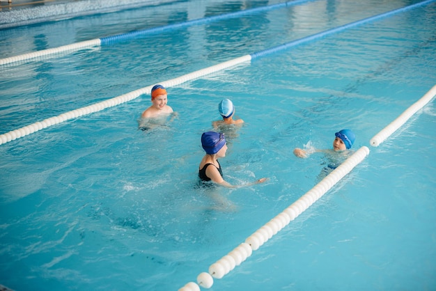 Un gruppo di ragazzi e ragazze si allena e impara a nuotare in piscina con un istruttore. Sviluppo di sport per bambini.