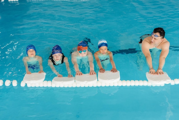 Un gruppo di ragazzi e ragazze si allena e impara a nuotare in piscina con un istruttore. Sviluppo di sport per bambini.