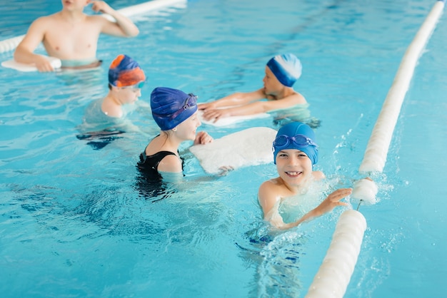 Un gruppo di ragazzi e ragazze si allena e impara a nuotare in piscina con un istruttore