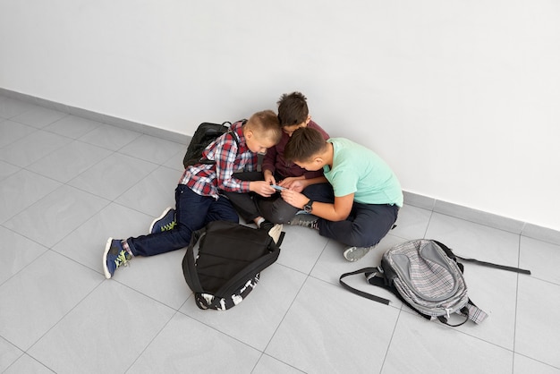 Un gruppo di ragazzi seduti sul corridoio della scuola sul pavimento, guardando, discutendo insieme o mostrando qualcosa.