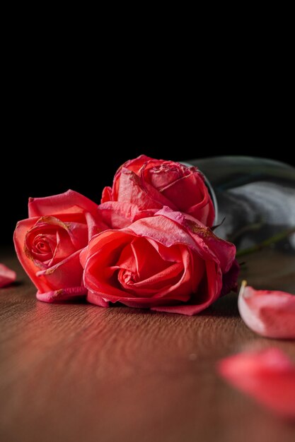 Un gruppo di rose rosa mette in un bicchiere di champagne che cade sul tavolo di legno di colore scuro