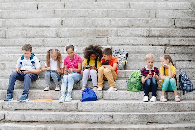 Un gruppo di scolari in abiti colorati è seduto sui gradini e guarda i gadget. Sette compagni di classe di diverse nazionalità.