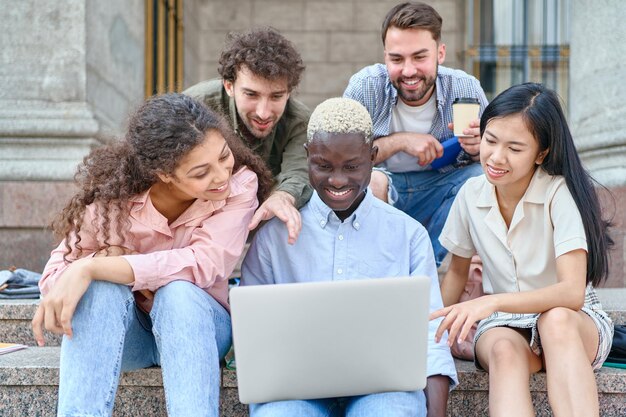 Un gruppo di studenti con laptop si siede sui gradini vicino al campus