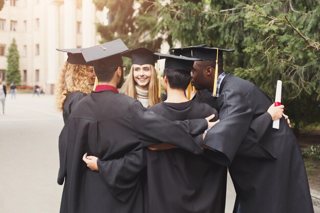 Un gruppo di studenti multietnici che si abbracciano per la laurea. Istruzione, qualifica e concetto di abito.