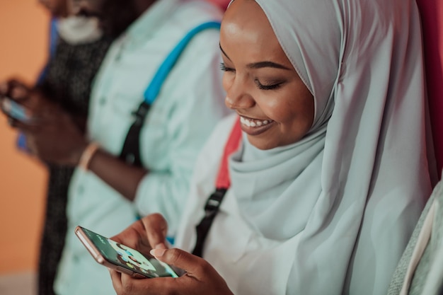 Un gruppo di studenti musulmani africani che utilizzano smartphone mentre si trovano di fronte a uno sfondo giallo. Foto di alta qualità