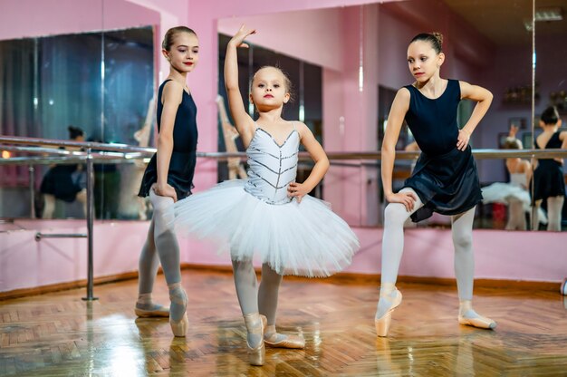 Un gruppo di tre piccoli ballerini di balletto in tutu in piedi in posa sulla sala da ballo. Giovani ballerini in uno studio con pavimento in legno e specchi.