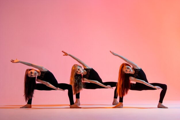 Un gruppo di tre ragazze di balletto in abiti attillati neri che ballano su uno sfondo rosso