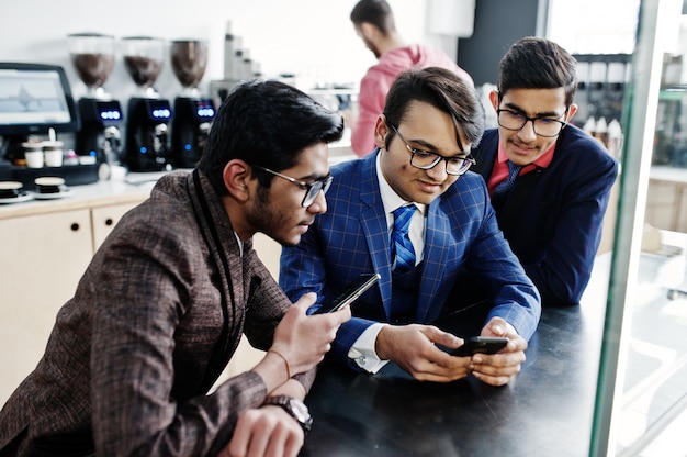 Un gruppo di tre uomini d'affari indiani in giacca e cravatta seduto sul caffè e guardando sul telefono cellulare.