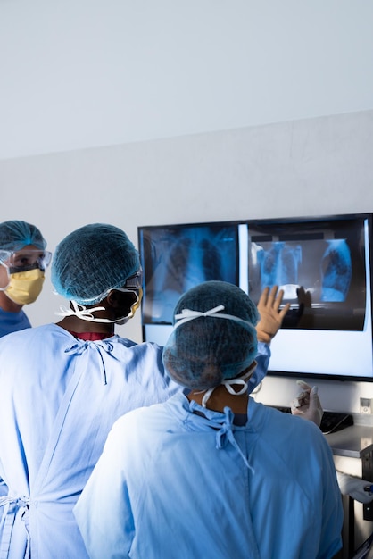 Un gruppo diversificato di chirurghi che discutono dei raggi X sullo schermo in sala operatoria, spazio di copia. Chirurgia, lavoro di squadra, ospedale, servizi medici e sanitari.