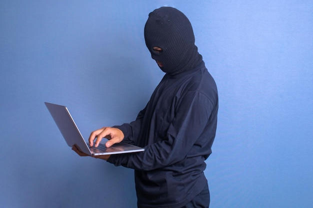 Un hacker ladro che ruba dati da un computer portatile isolato sullo sfondo blu dello studio