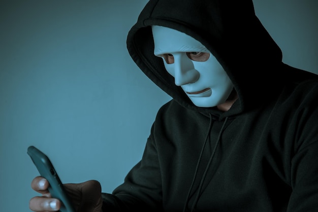 Un hacker mascherato anonimo utilizza uno smartphone per penetrare le informazioni finanziarie della carta di credito Concetto di hacking e malware