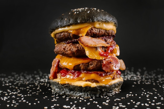 Un hamburger nero molto grande con tre cotolette sullo sfondo nero