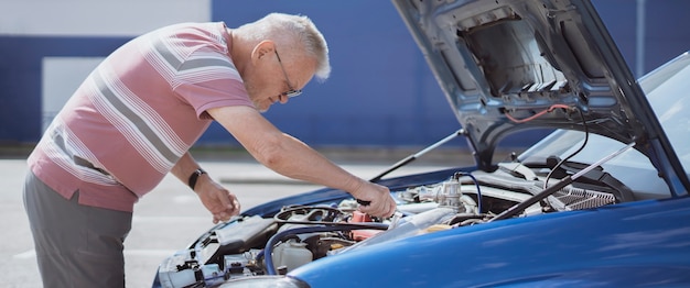 Un hobby dell'uomo anziano, persona anziana che ripara il motore dell'auto all'aperto