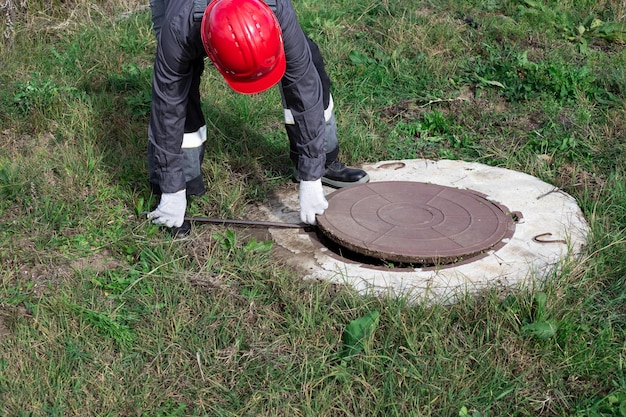 Un idraulico maschio apre un pozzo d'acqua con un piede di porco Ispezione e riparazione di pozzi d'acqua e fosse settiche