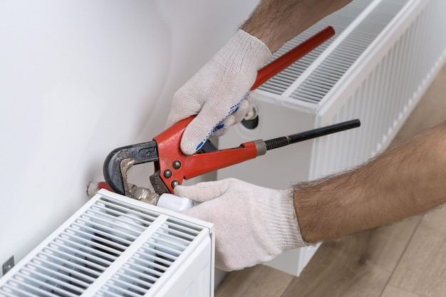 Un idraulico maschio installa un radiatore nel sistema di riscaldamento di un appartamento