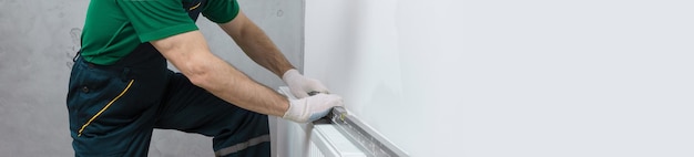 Un idraulico maschio installa un radiatore nell'impianto di riscaldamento di un appartamento Ragazzo in tuta e chiave a gas