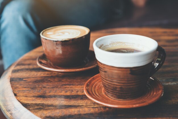 Un'immagine del primo piano di due tazze di caffè caldo del latte e caffè nero sulla tavola di legno d'annata in caffè