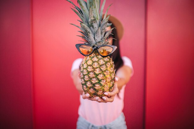 Un'immagine della ragazza tiene l'ananas. Si fa vedere dalla telecamera. Ha gli occhiali.