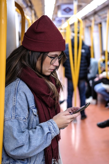 Un'immagine verticale di una donna hipster in abiti invernali che controlla il telefono