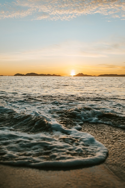 Un'immagine verticale di una marea sulla spiaggia sulla sabbia durante un tramonto colorato