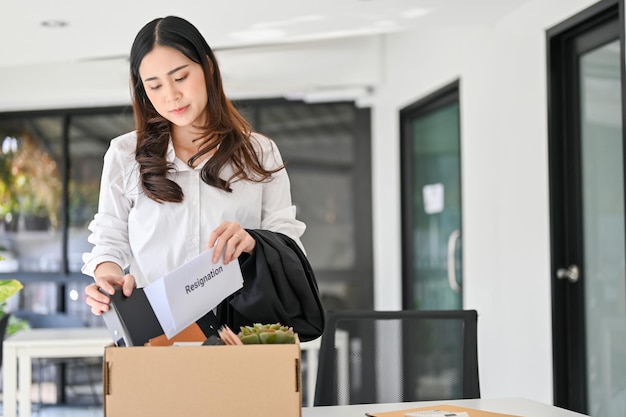 Un'impiegata asiatica triste che impacchetta la sua roba in una scatola di cartone nell'ufficio che lascia il lavoro