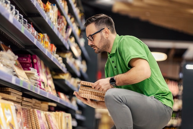Un impiegato di un supermercato è accovacciato accanto a uno scaffale e mostra generi alimentari al mercato