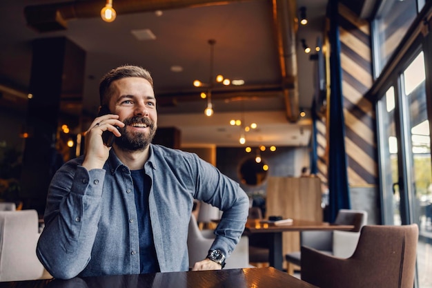 Un imprenditore sorridente è seduto in una caffetteria e parla al telefono con un socio in affari