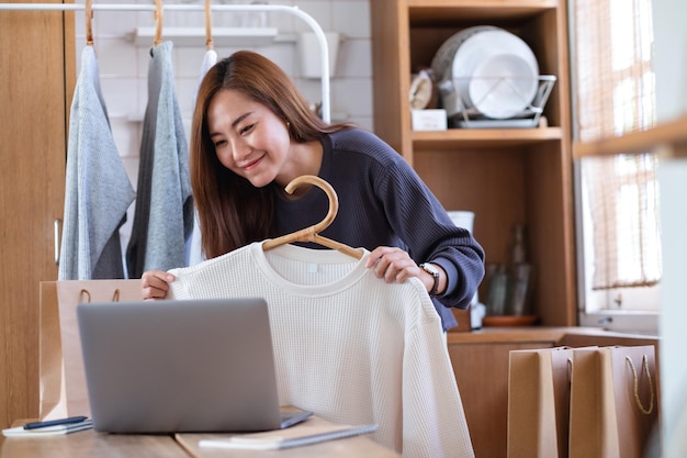 Un'imprenditrice che utilizza un computer portatile per vendere vestiti online o recensire il prodotto sui social media a casa